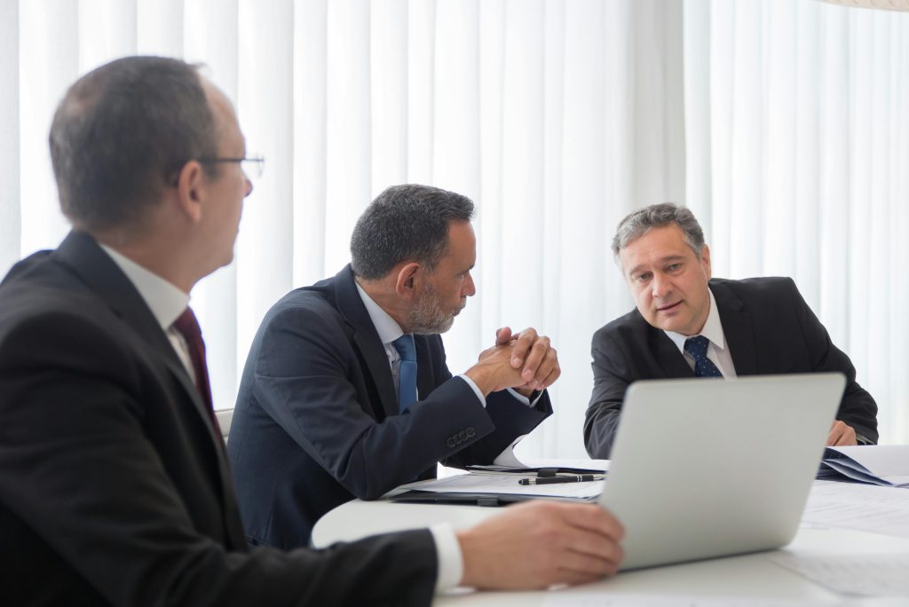 Three businessmen collaborating during a meeting around a laptop in a bright office.